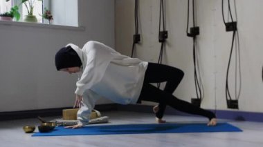 Yoga minderinde yoga egzersizi yapan tesettürlü genç bir kadın.