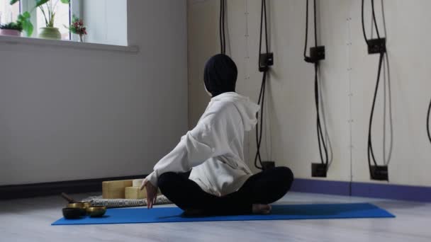 A young woman in hijab sitting on yoga mat and leaning down — Stock Video