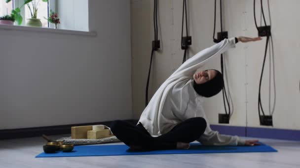 A young woman in hijab sitting on yoga mat and leaning to the sides — Stock Video