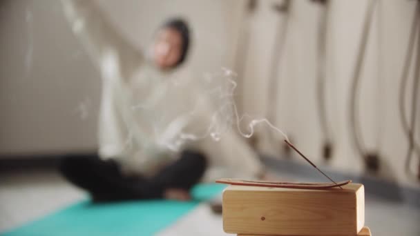 Yoga - a young woman in a hijab doing yoga with a smoldering incense on the foreground — Stock Video