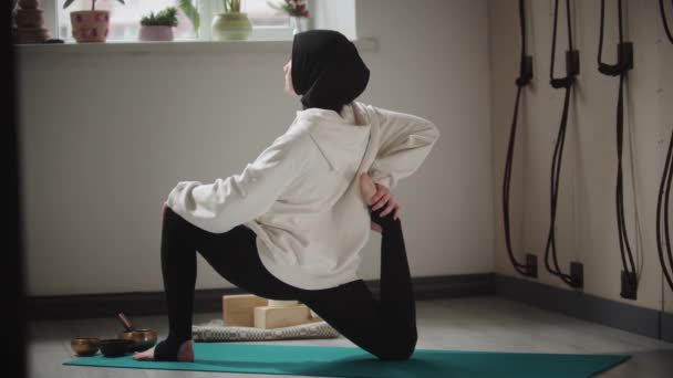 Yoga indoors - young woman in hijab doing stretching exercises on yoga mat — Stock Video