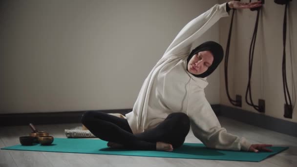 Jóga - mladá žena v hidžábu dělá strečink cvičení obklopen předměty pro meditaci — Stock video