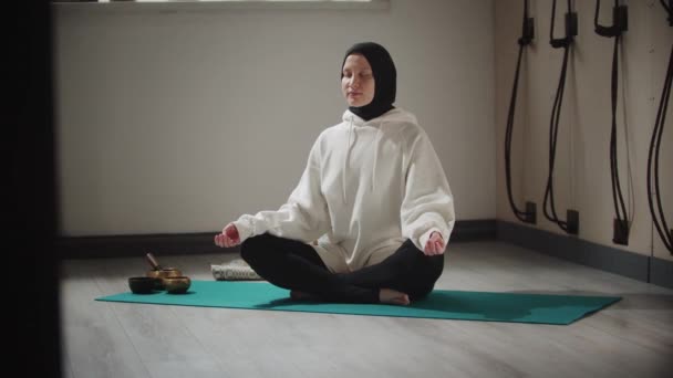 योग हिजाब में युवा महिला ध्यान के लिए वस्तुओं से घिरा योग कर रही है — स्टॉक वीडियो