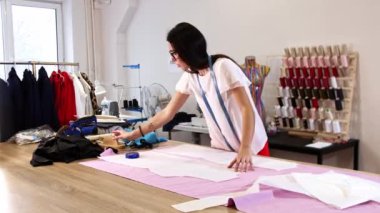 Bir kadın masanın üzerindeki pembe örtüyü kalıplara göre kesmek için hazırlıyor.