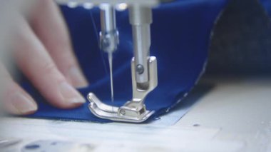 Dikiş makinesiyle lacivert kumaş dikiyorum. Orta çekim
