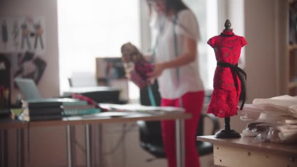 Een kleine steekproef van een jurk op een kleine etalagepop en vrouw die in een ontwerpstudio werkt — Stockvideo