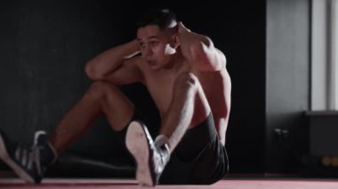 Formda genç bir adam spor salonunda karın kaslarına vuruyor. Orta çekim