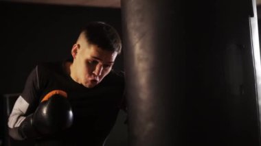 Boks antrenmanı. Boks eldiveni giyen agresif sporcu kum torbasına yumruk atıyor. Orta çekim