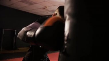 Boks eğitimi. Kısa saçlı, formda bir adam kum torbasını yavaş çekimde yumrukluyor. Orta çekim