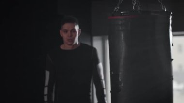 Spor elbiseli genç bir adam kum torbasına doğru yürür ve antrenman için hazırlanır. Orta çekim