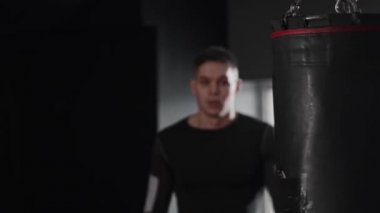 Boks eldivenli genç adam elleriyle yüzünü kapatıyor ve kameraya bakıyor. Orta çekim