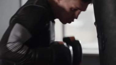 Spor elbiseli genç adam kum torbasına vuruyor. Orta çekim