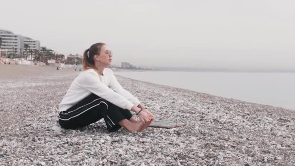 一个女人坐在海滨 跪在脚趾头上 然后踩到了沙河的木板上 — 图库视频影像