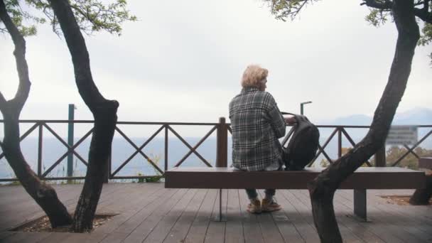 年轻时髦的男人坐在长椅上 把背包从背靠着大海的地方搬开 — 图库视频影像