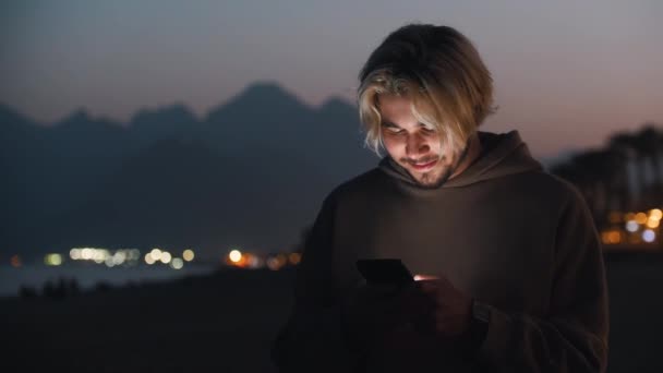 Homem Loiro Com Capuz Bege Enviando Mensagens Seu Telefone Olhando — Vídeo de Stock