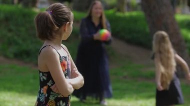 Ailesi top oynarken küçük bir kız kenara çekiliyor ve alınıyor. Ona sesleniyorlar ve annesine koşuyor. Orta çekim