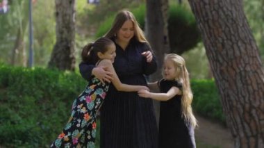 Parkta birbirine sarılan anne ve iki kızın mutlu ailesi. Orta çekim