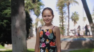 Parkta durup kameraya bakan sevimli, gülümseyen kız. Orta çekim