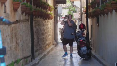 Genç bir adam sokaklarda yürüyor ve çevrenin fotoğraflarını çekiyor. Orta çekim