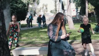 İki küçük kız telefonuyla annelerinin yanına koşup onu oynamaya zorluyor. Orta çekim