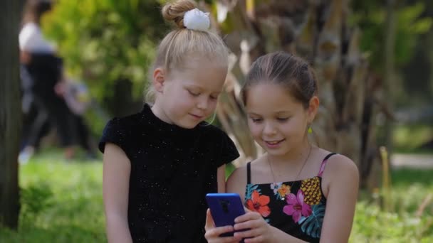 Две Маленькие Девочки Сестры Сидят Траве Играют Телефоном Средний Выстрел — стоковое видео