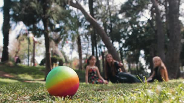 母亲的家人和两个女儿坐在草地上 其中一个女孩从前面拿起橡皮球 — 图库视频影像