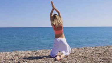 Sarışın kadın denize bakan çakıl taşı plajında yoga egzersizi yapıyor. Orta çekim