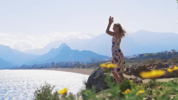 大人の女性は海のそばの岩の上に立ってヨガの練習をしています ミッドショット — ストック動画
