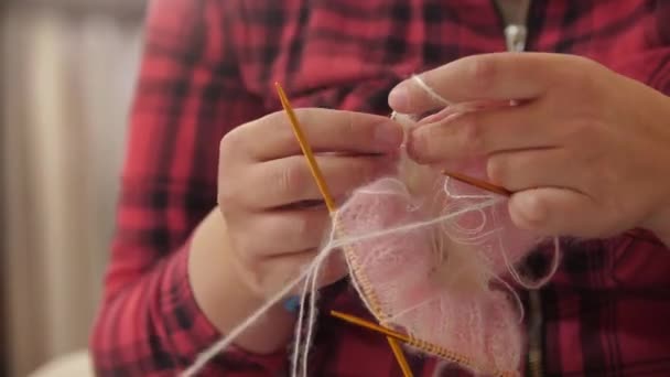 赤い再生シャツの女性は薄いピンクの糸から服の一部を編んでいます ミッドショット — ストック動画