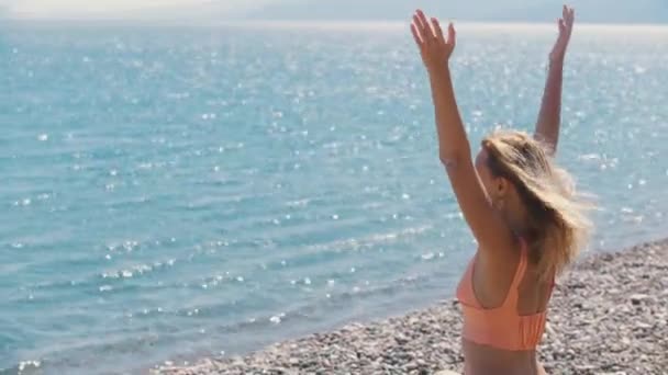 海によって小石のビーチで瞑想大人の精神的なブロンドの女性 ミッドショット — ストック動画