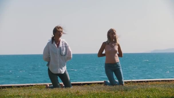 海のそばで簡単な体操をする大人の女性2人 ミッドショット — ストック動画