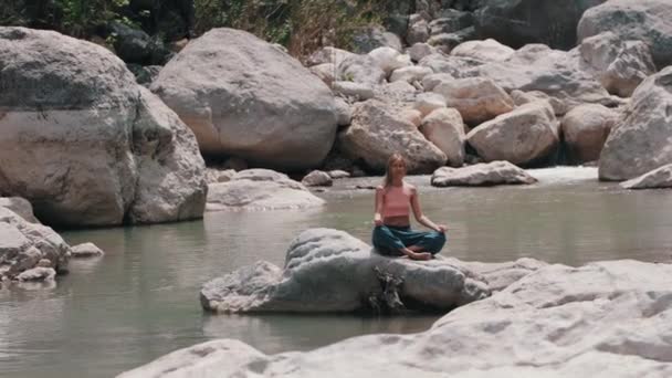 小川の真ん中の岩の上で瞑想する女性 ミッドショット — ストック動画