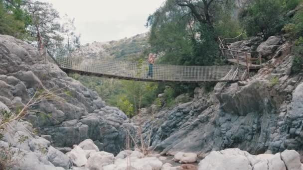 水流の上のロープ橋の上のブロンドの女性 ミッドショット — ストック動画