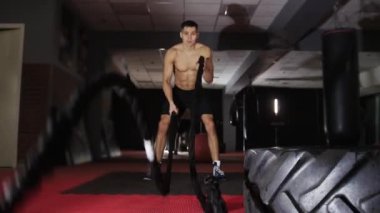 Fitness eğitimi - formda olmayan bir adam halatlara vurarak çapraz egzersiz yapıyor. Orta çekim