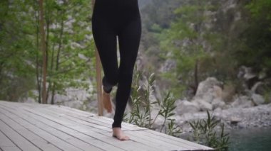 Dağlarda yoga yapan siyah elbiseli bir kadın jimnastik yapıyor. Orta çekim