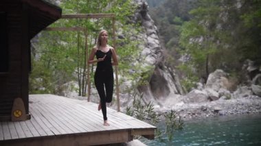 Dağlarda yoga yapan siyah elbiseli bir kadın basit jimnastik egzersizleri yapıyor. Orta çekim