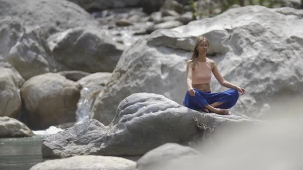 ヨガの水の流れ 女性は岩の上に座って瞑想 ミッドショット — ストック動画