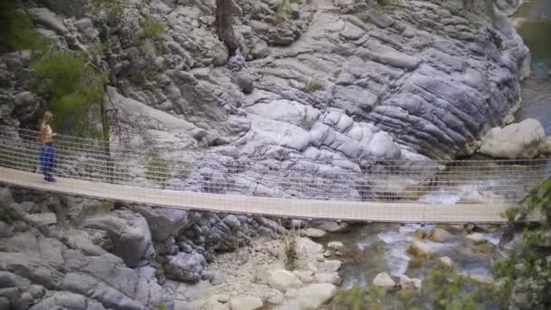 在岩石和水流之上的缆桥上行走的成年妇女 — 图库视频影像