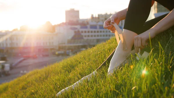 バレリーナネクタイアップ彼女のポイントシューズ上の緑の芝生の上に座って丘の上 ミッドショット — ストック写真
