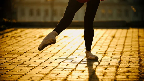 Feet of young woman ballerina dancing on the roof in the pointe shoes - yellow sunset. Mid shot