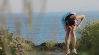 Spor, deniz kenarındaki yoga minderinde duran ve vücudunu esneten bir kadın. Orta çekim