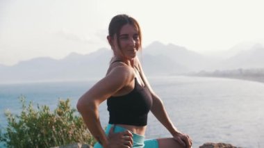 Gülümseyen sportif kadın tepede duruyor ve elini kameraya uzatıyor. Orta çekim