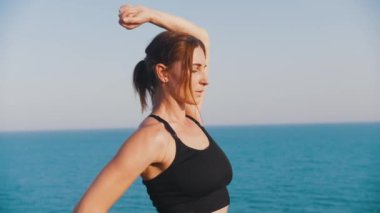 Spor bluzlu gülümseyen kadın denizin kenarındaki tepede duruyor. Orta çekim