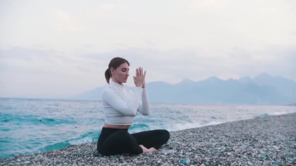 Woman Sits Pebble Beach Lotus Position Leaning Forwards Sea Mid — Vídeos de Stock