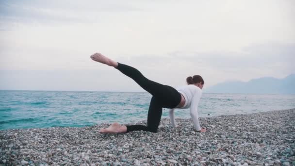 Женщина Белом Свитере Делает Спортивные Упражнения Галечном Пляже Средний Выстрел — стоковое видео