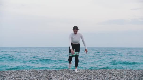 Женщина Тренируется Эластичной Лентой Между Ног Галечном Пляже Моря Средний — стоковое видео