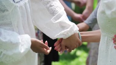 Women in traditional light dresses holding hands during the festival. Mid shot