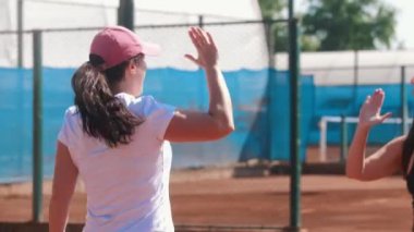 Tennis students give five to their coach above the net on the court. Mid shot