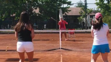 Tenis koçu öğrencilerini tenis kortunda çalıştırıyor. Orta çekim