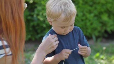 A little boy with his red-haired mom playing with a dandelion stalk. Mid shot